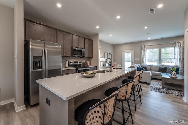 kitchen with dark brown cabinetry, appliances with stainless steel finishes, a sink, light wood-style floors, and visible vents