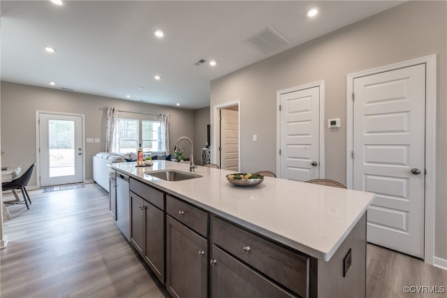 kitchen featuring visible vents, open floor plan, an island with sink, a sink, and light wood-style flooring