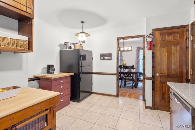 kitchen featuring stainless steel dishwasher, freestanding refrigerator, baseboards, light tile patterned floors, and hanging light fixtures