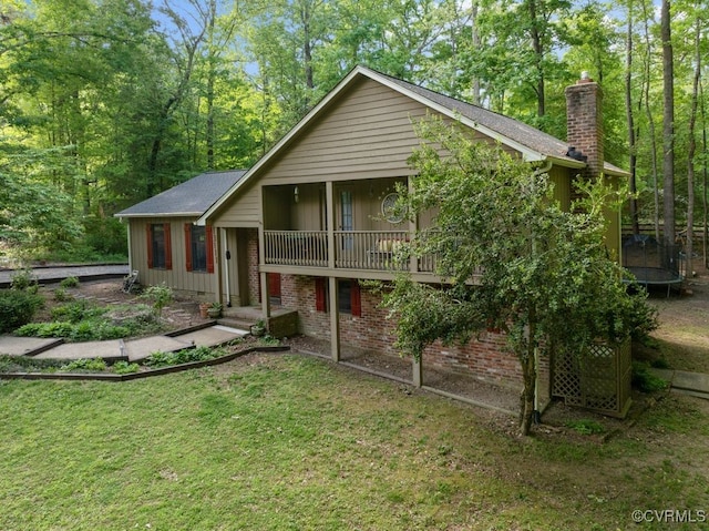view of front of house with a trampoline, a chimney, a front yard, and brick siding
