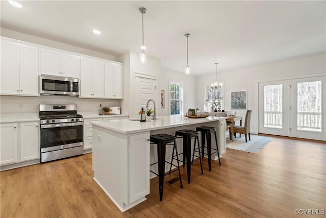 kitchen featuring a kitchen island with sink, appliances with stainless steel finishes, a sink, light countertops, and light wood-style flooring