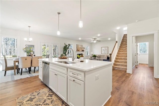 kitchen featuring white cabinets, a sink, light wood-style floors, dishwasher, and pendant lighting