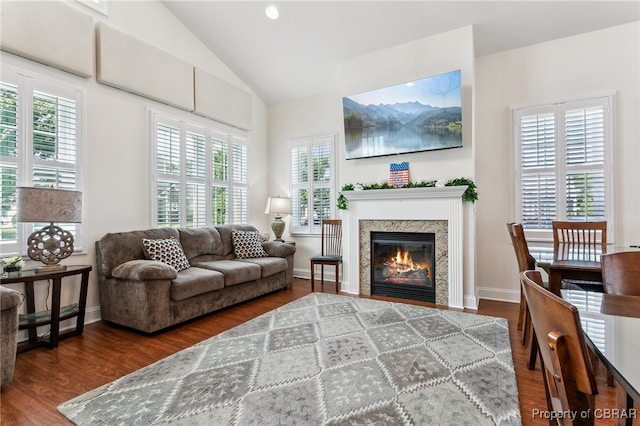 living area featuring a baseboard heating unit, a glass covered fireplace, wood finished floors, and lofted ceiling