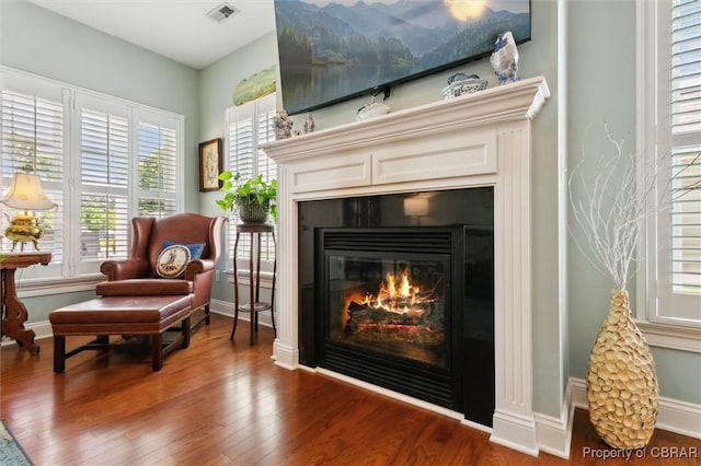 living area featuring a glass covered fireplace, plenty of natural light, wood finished floors, and visible vents