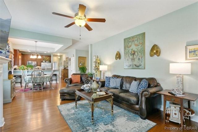 living room with a raised ceiling, ceiling fan with notable chandelier, and wood finished floors