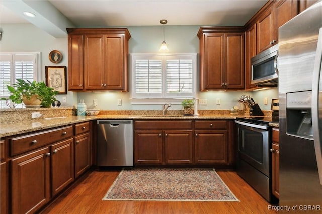 kitchen featuring dark wood-style flooring, appliances with stainless steel finishes, hanging light fixtures, light stone countertops, and a sink