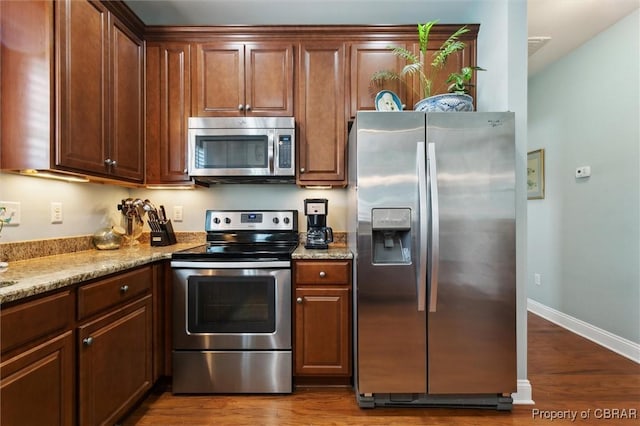 kitchen with light stone countertops, appliances with stainless steel finishes, baseboards, and dark wood-type flooring