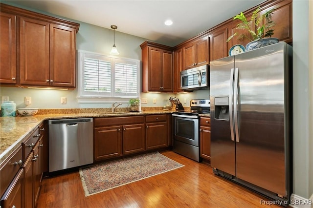 kitchen featuring decorative light fixtures, appliances with stainless steel finishes, a sink, and wood finished floors