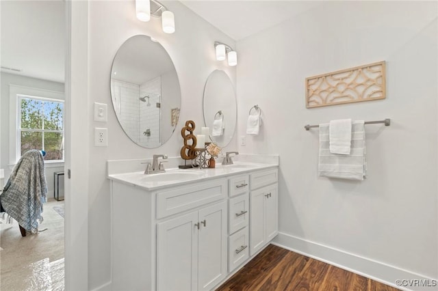 bathroom featuring a sink, tiled shower, baseboards, and double vanity