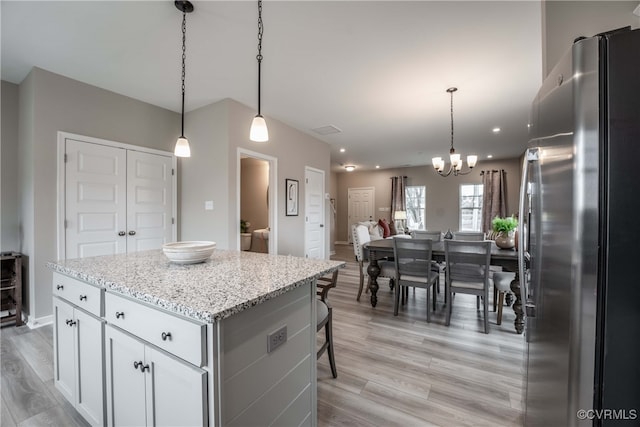 kitchen with a kitchen island, light wood-type flooring, light stone counters, freestanding refrigerator, and a notable chandelier