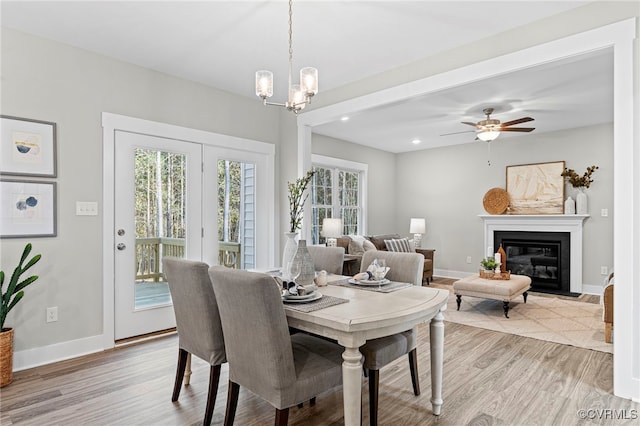 dining space with baseboards, a glass covered fireplace, and light wood finished floors