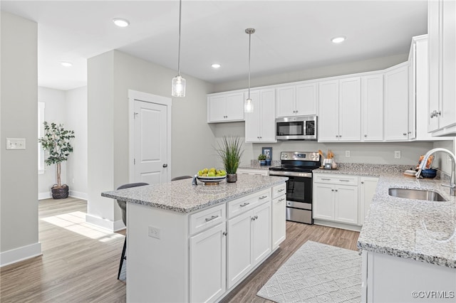 kitchen with a kitchen island, appliances with stainless steel finishes, a sink, baseboards, and white cabinets