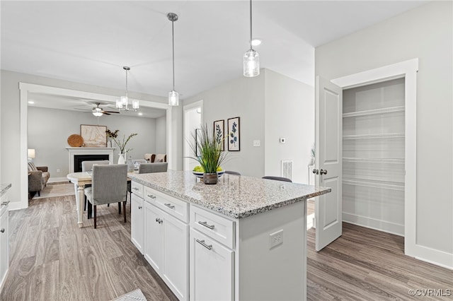 kitchen featuring ceiling fan, decorative light fixtures, a center island, wood finished floors, and white cabinetry
