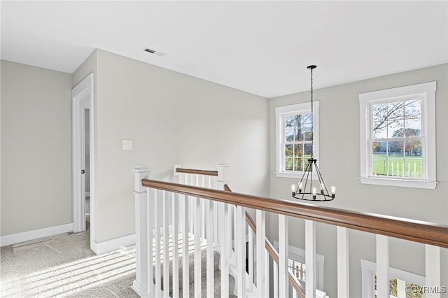hallway with visible vents, baseboards, carpet flooring, a notable chandelier, and an upstairs landing