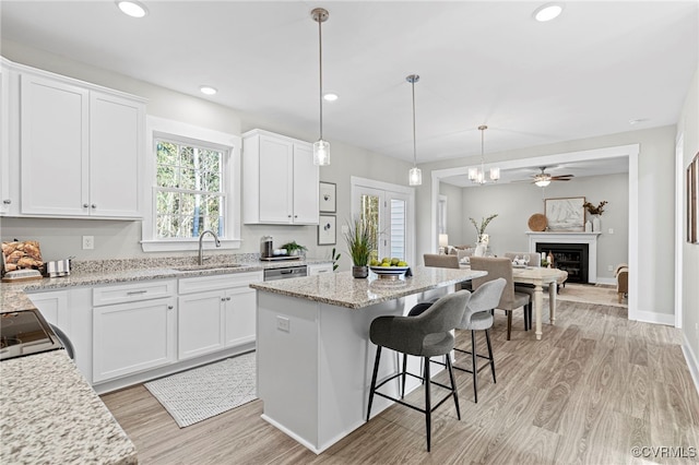 kitchen featuring a sink, light wood finished floors, open floor plan, a breakfast bar, and white cabinetry