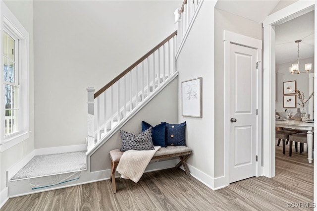 stairway featuring baseboards, wood finished floors, and an inviting chandelier
