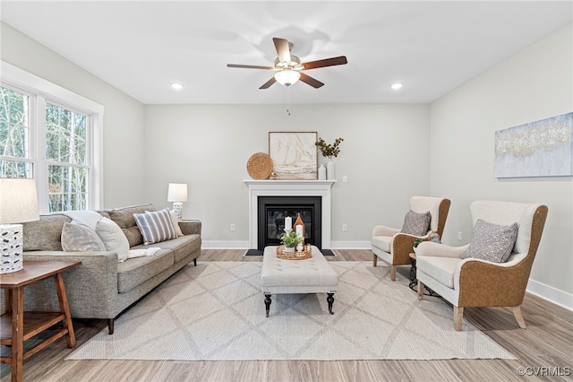 living area with a ceiling fan, a fireplace with flush hearth, wood finished floors, baseboards, and recessed lighting