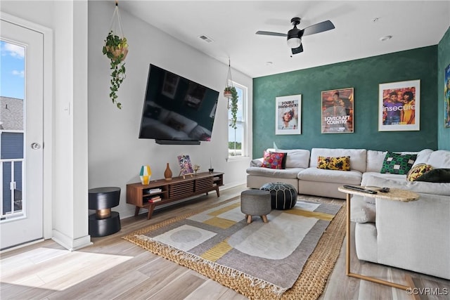 living room with ceiling fan, visible vents, wood finished floors, and an accent wall