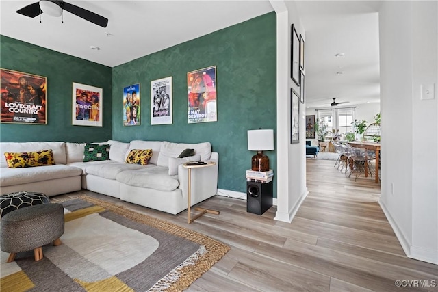 living area with wood finished floors, baseboards, ceiling fan, and an accent wall