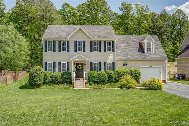 colonial home with a front yard, aphalt driveway, an attached garage, and fence