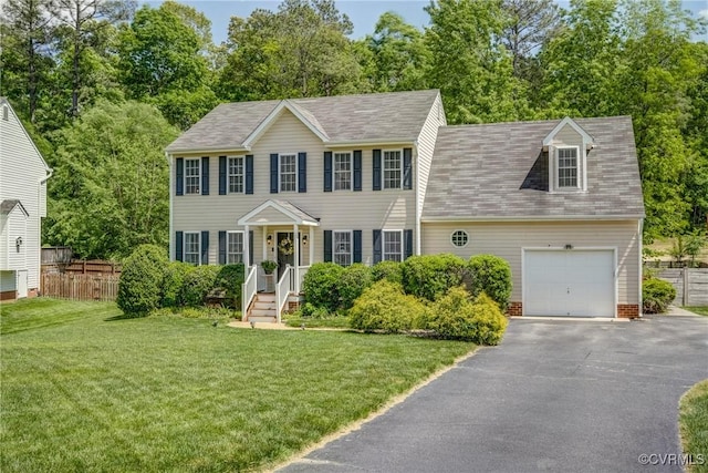 colonial home featuring roof with shingles, driveway, fence, and a front yard