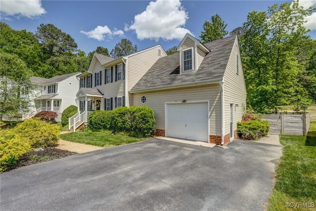 colonial inspired home with aphalt driveway, a garage, and fence