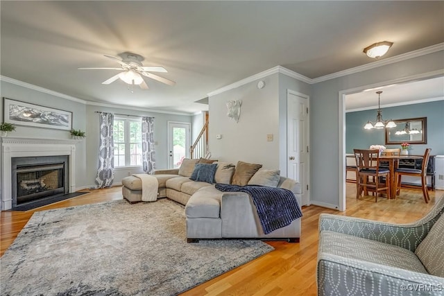 living room featuring light wood-style floors, crown molding, and ceiling fan with notable chandelier