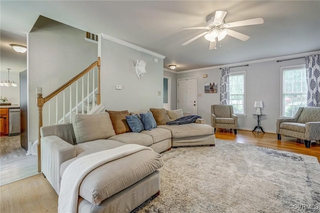 living room with stairway, crown molding, light wood-style flooring, and a ceiling fan