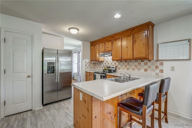 kitchen featuring a sink, brown cabinetry, light countertops, decorative backsplash, and appliances with stainless steel finishes
