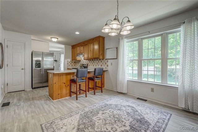 kitchen with a peninsula, brown cabinetry, stainless steel refrigerator with ice dispenser, visible vents, and a notable chandelier