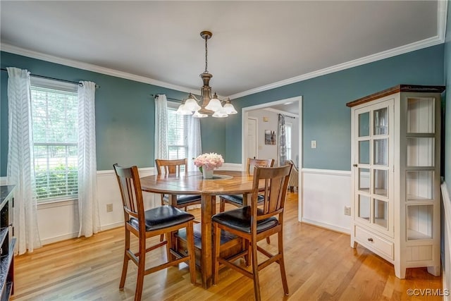 dining area featuring crown molding, light wood-style floors, a wainscoted wall, and a notable chandelier