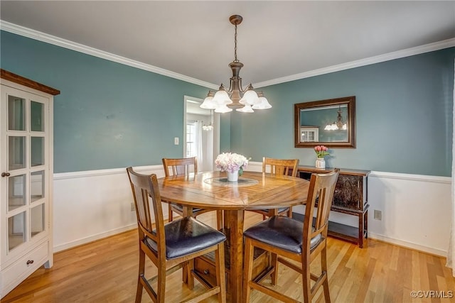 dining room with a wainscoted wall, an inviting chandelier, crown molding, and light wood-type flooring