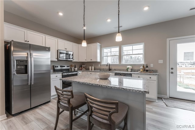 kitchen featuring white cabinets, light stone countertops, light wood finished floors, a breakfast bar area, and stainless steel appliances