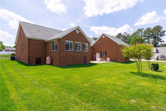 back of property featuring a lawn, brick siding, central AC unit, and a patio area