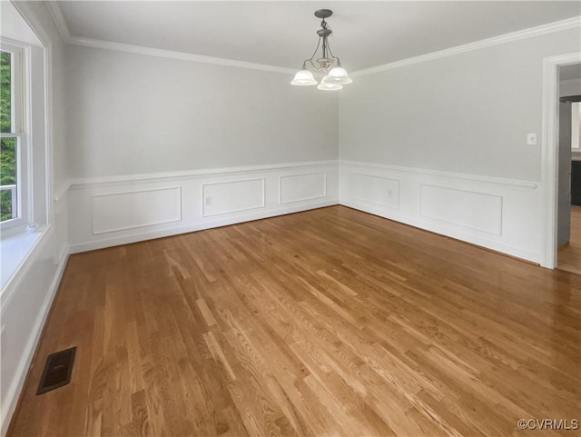spare room featuring visible vents, a wainscoted wall, a chandelier, ornamental molding, and light wood-style flooring
