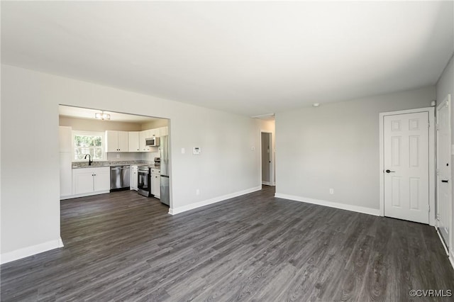 unfurnished living room with baseboards, a sink, and dark wood-style floors