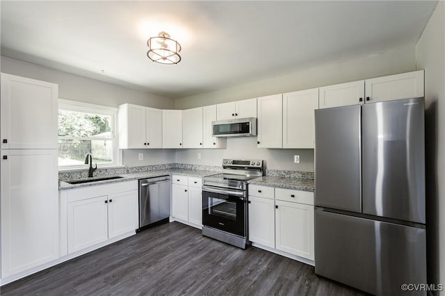 kitchen with light stone countertops, dark wood-type flooring, white cabinetry, a sink, and appliances with stainless steel finishes