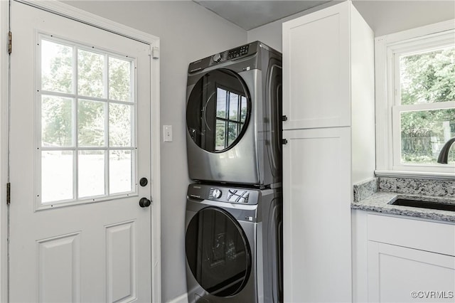 laundry room featuring a sink, stacked washer and clothes dryer, cabinet space, and a healthy amount of sunlight