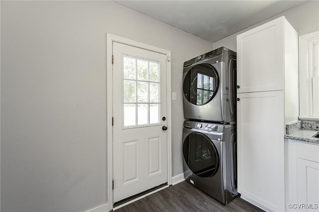 laundry area featuring cabinet space, stacked washer and dryer, baseboards, and dark wood finished floors
