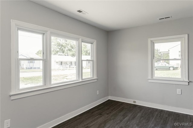empty room with visible vents, dark wood-style flooring, and baseboards