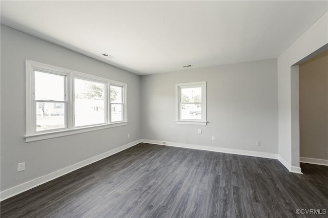unfurnished room with baseboards, visible vents, and dark wood-type flooring