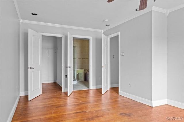 unfurnished bedroom featuring a walk in closet, crown molding, light wood finished floors, baseboards, and a closet