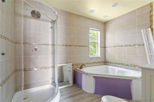 bathroom with tile walls, a shower stall, wood finished floors, a bath, and toilet