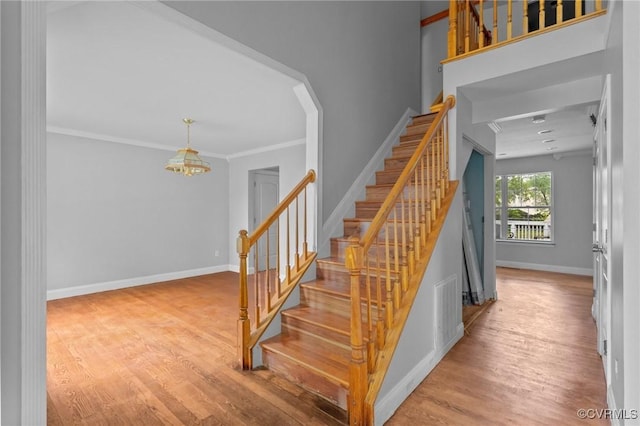 stairway with a chandelier, wood finished floors, baseboards, and ornamental molding