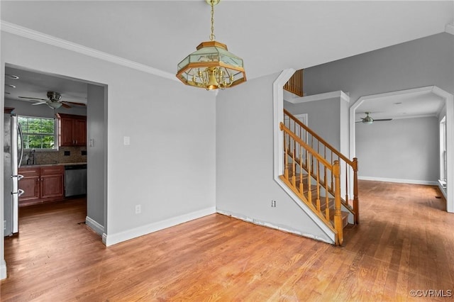 unfurnished dining area featuring ceiling fan, stairway, wood finished floors, baseboards, and ornamental molding