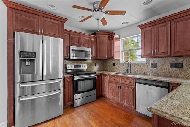 kitchen featuring stainless steel appliances, a sink, light wood-style flooring, backsplash, and ceiling fan
