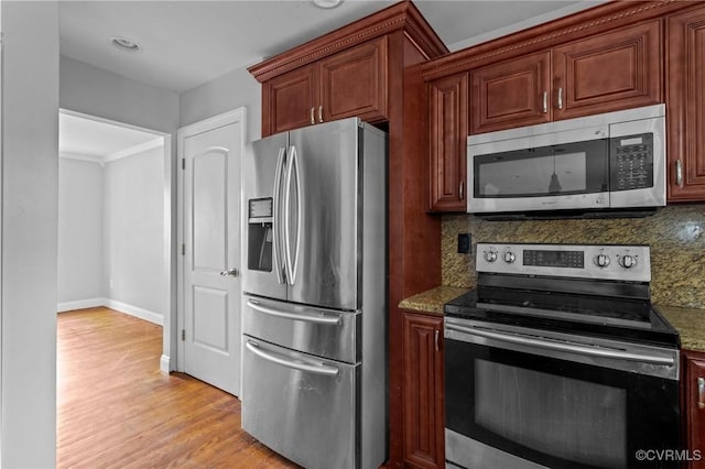 kitchen featuring appliances with stainless steel finishes, backsplash, light wood-style floors, and dark stone counters