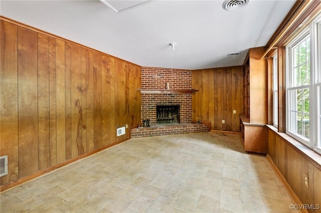 unfurnished living room with a brick fireplace, wood walls, and visible vents