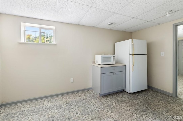 kitchen featuring white appliances, baseboards, a drop ceiling, and light floors