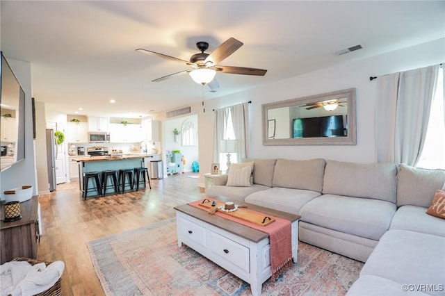 living room featuring visible vents, a ceiling fan, and light wood-style floors